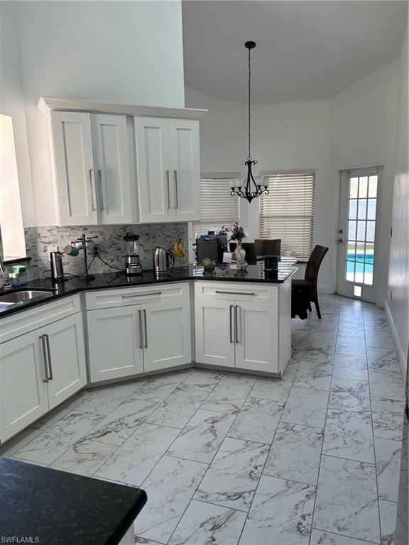 Kitchen featuring light marble finish floors, dark stone countertops, white cabinetry, a peninsula, and a high ceiling
