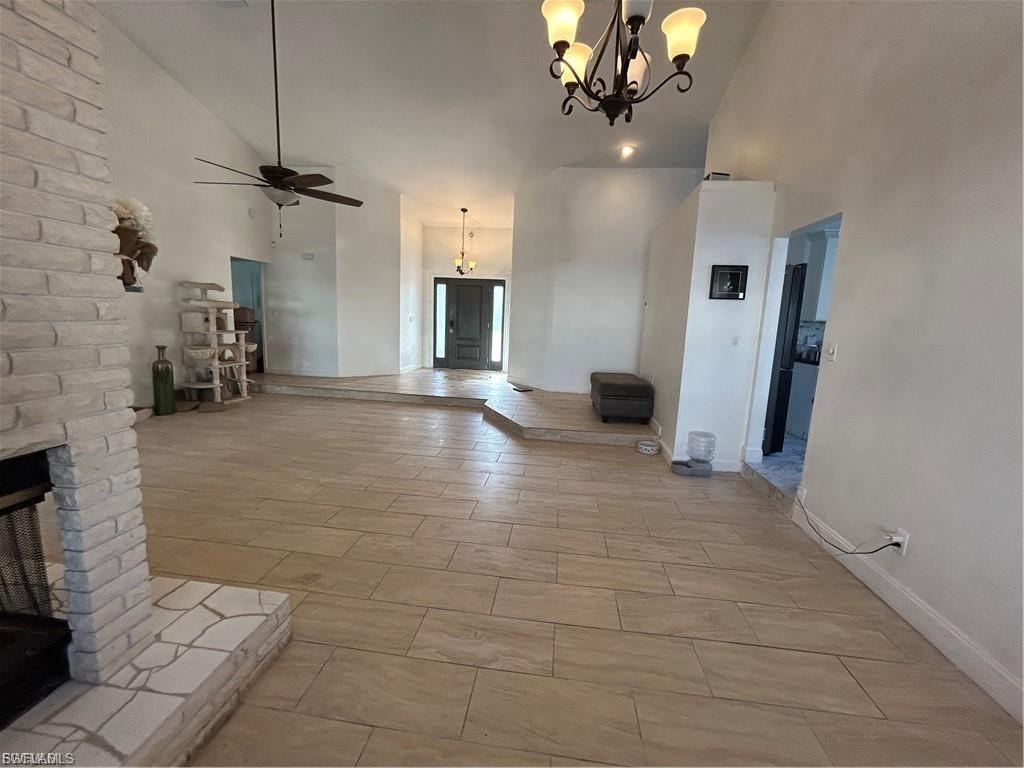 Unfurnished living room with vaulted ceiling, a ceiling fan, hanging lights, and a fireplace