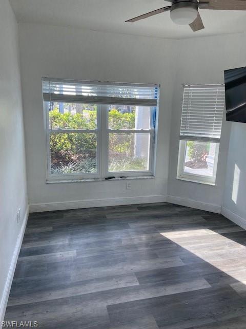 Spare room with dark wood-style floors, ceiling fan, and healthy amount of natural light