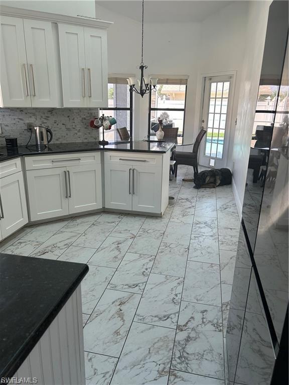 Kitchen with light marble finish floors, dark stone countertops, suspended lighting, white cabinetry, and vaulted ceiling