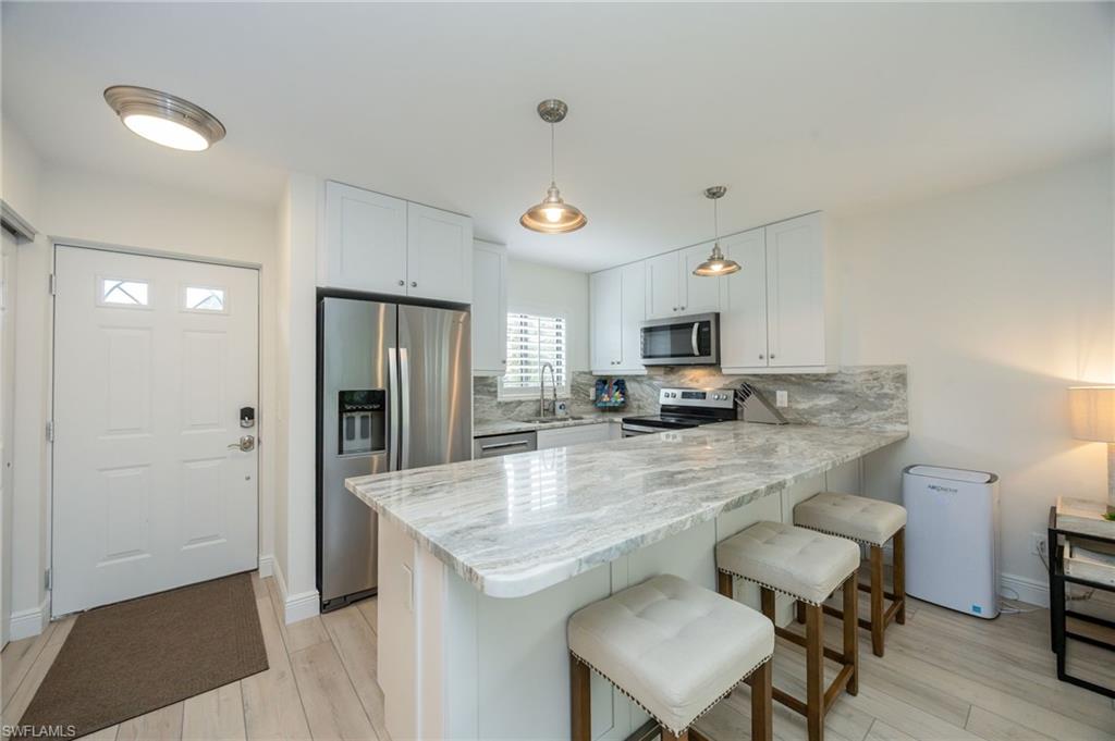 Kitchen featuring white cabinetry, stainless steel appliances, a stone countertop, island seating, and wood-finish flooring