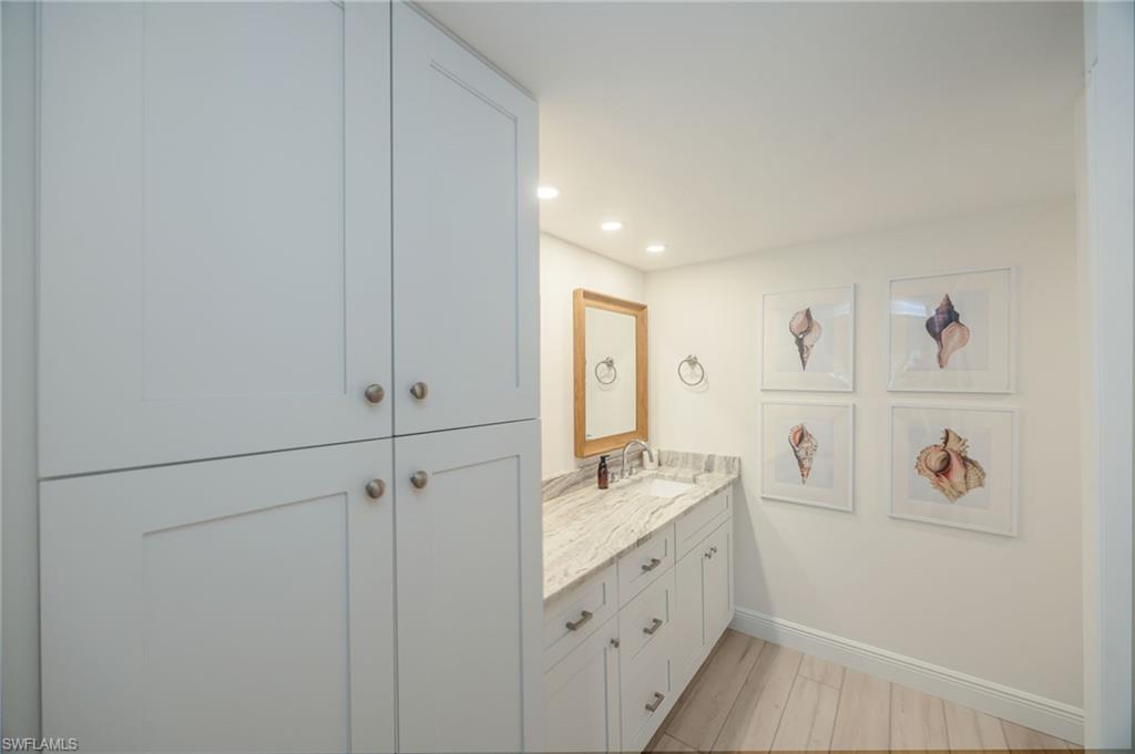 White shaker cabinetry, stone countertop, integrated sink, and wood-finish flooring