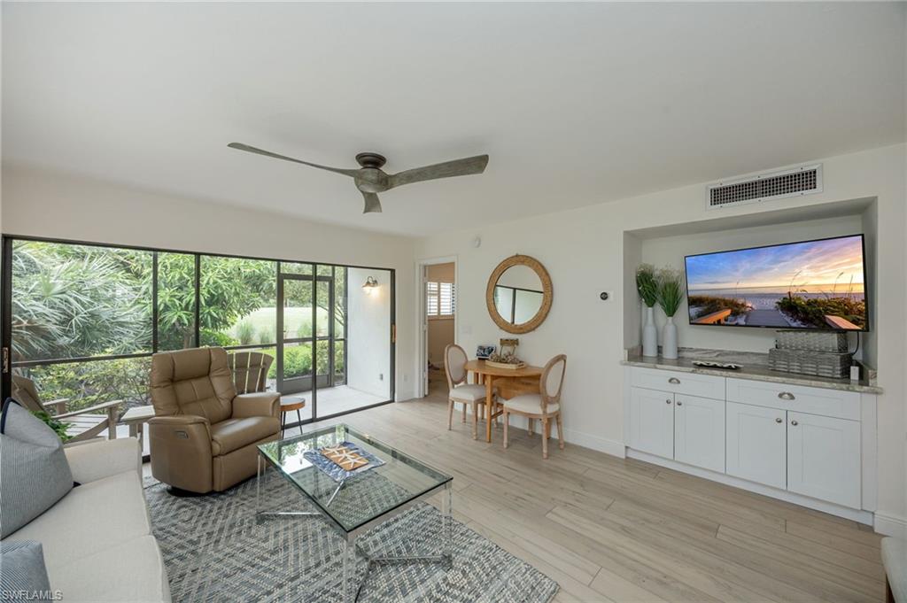 Full-height screened enclosure, wood-finish flooring, built-in cabinetry with light-colored countertops, integrated wall-mounted television niche, and a ceiling fan