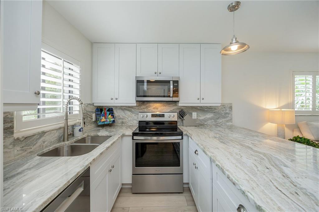 Kitchen featuring white shaker-style cabinetry, stainless steel appliances, a dual basin sink with gooseneck faucet, and light-toned, veined countertops with a matching backsplash