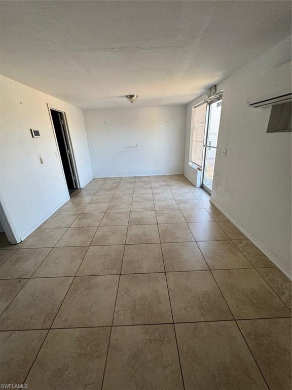 Tiled empty room with a wall unit AC and baseboards