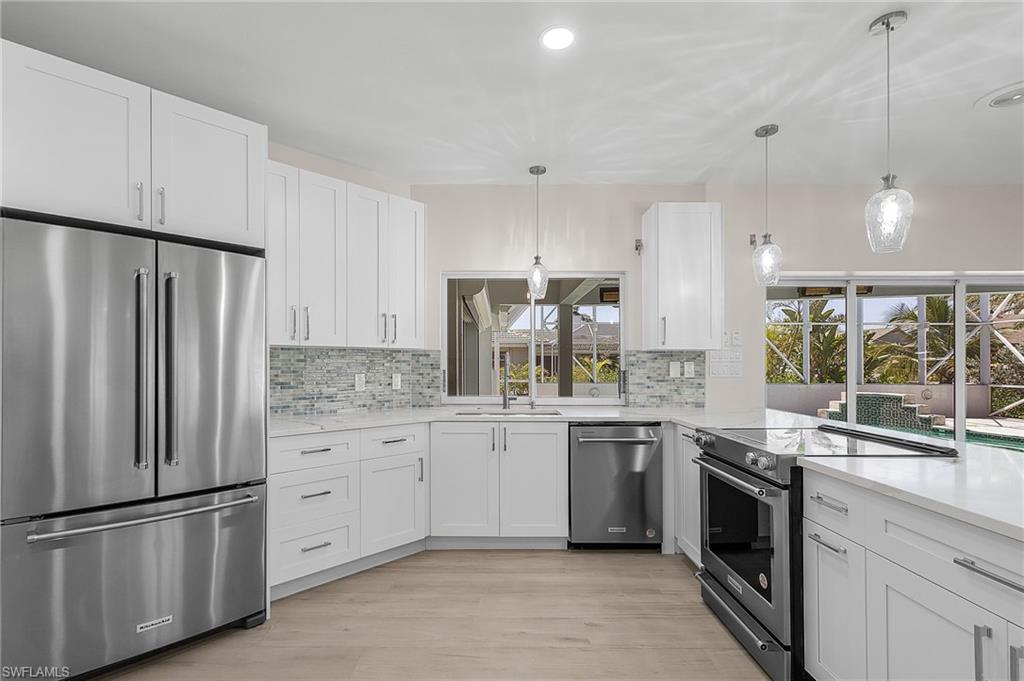 Kitchen featuring stainless steel appliances, white cabinetry, hanging light fixtures, light wood-style floors, and backsplash