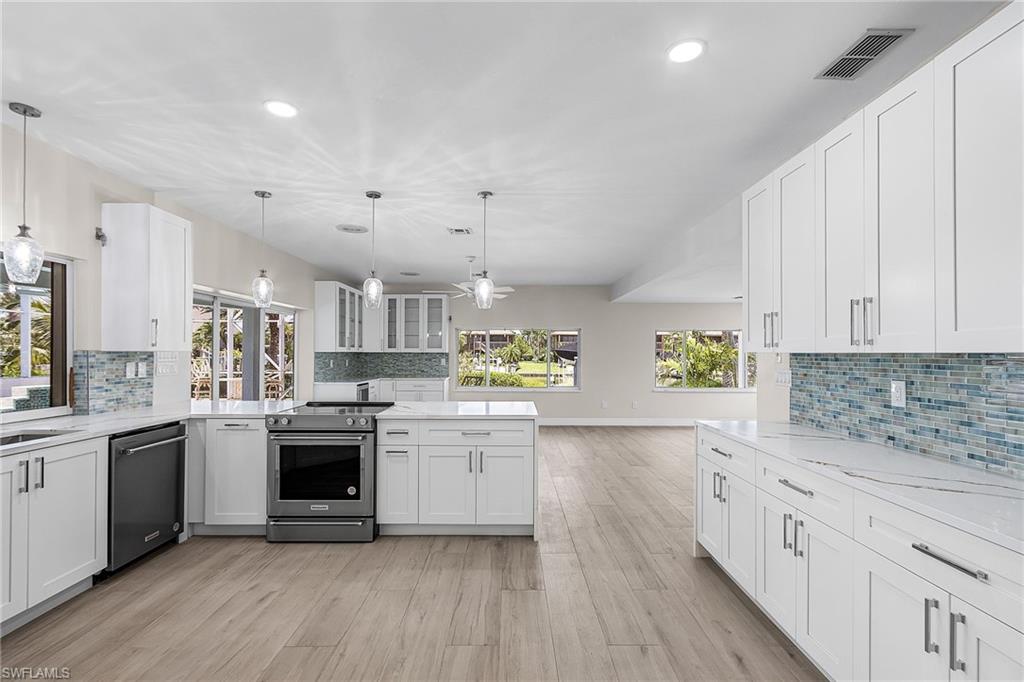 Kitchen featuring white cabinets, decorative backsplash, stainless steel appliances, and light stone counters