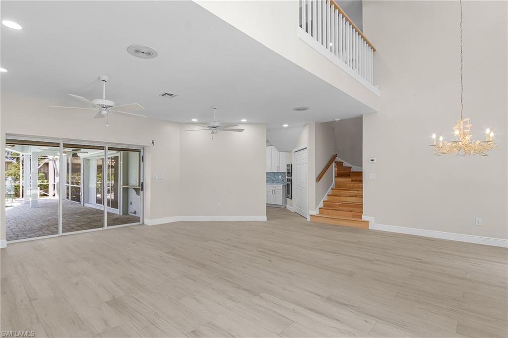 Unfurnished living room featuring light wood-style floors, a chandelier, ceiling fan, and a high ceiling