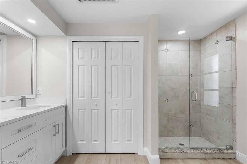 Bathroom with a closet, a stall shower, vanity, recessed lighting, and light wood-type flooring