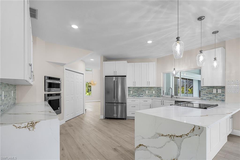 Kitchen with light stone countertops, decorative backsplash, white cabinetry, a peninsula, and high quality fridge