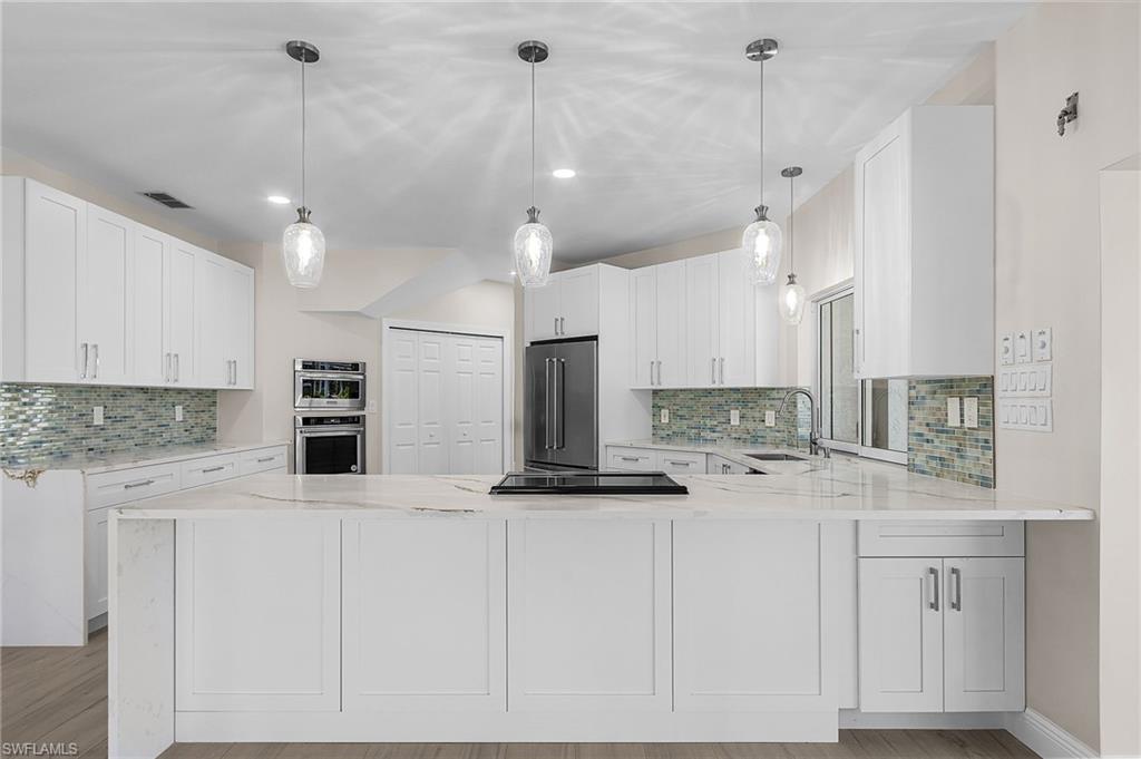 Kitchen featuring light stone countertops, pendant lighting, stainless steel appliances, and a peninsula