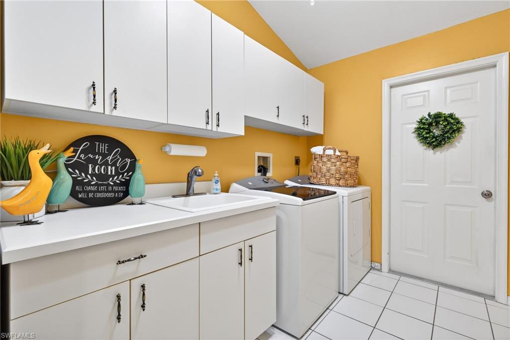 Laundry area featuring light tile patterned flooring, cabinet space, washing machine and dryer.
