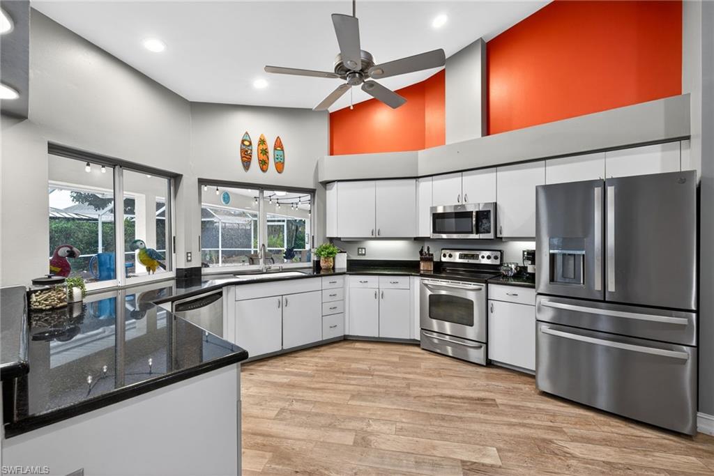 Kitchen with stainless steel appliances, a high ceiling, light wood-style flooring, white cabinets, and a ceiling fan