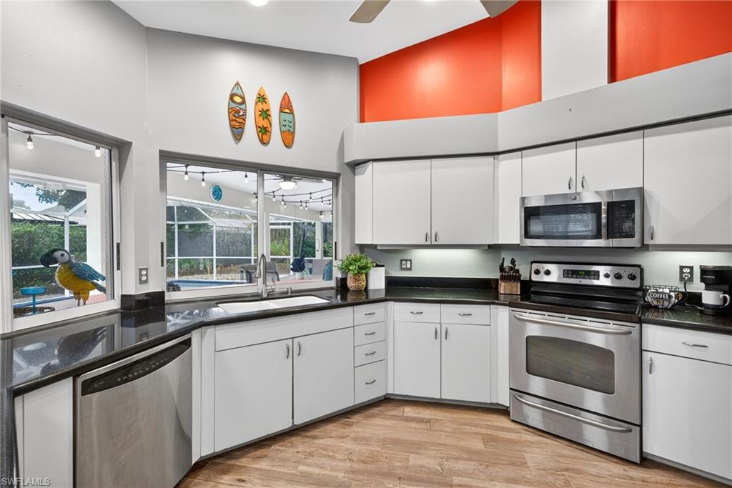 Kitchen with white cabinets, stainless steel appliances, light wood-style floors, a ceiling fan, and a high ceiling