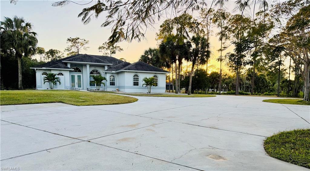 View of front facade featuring a front lawn, stucco siding, curved driveway, and view of scattered trees