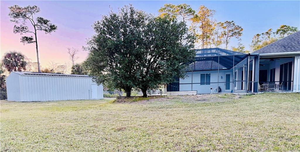 Rear view of house featuring glass enclosure, a lawn, an outdoor structure, a sunroom, and a patio