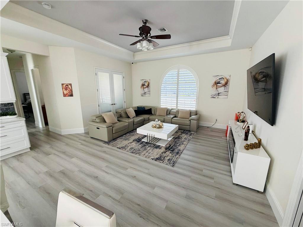 Living room with ceiling fan, light wood-style flooring, a tray ceiling, and ornamental molding