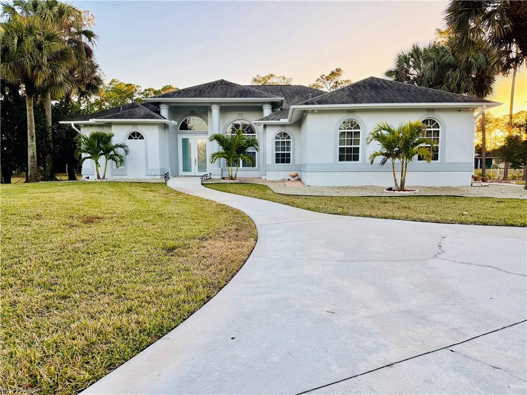 View of front of property with stucco siding, a yard, french doors, and a shingled roof