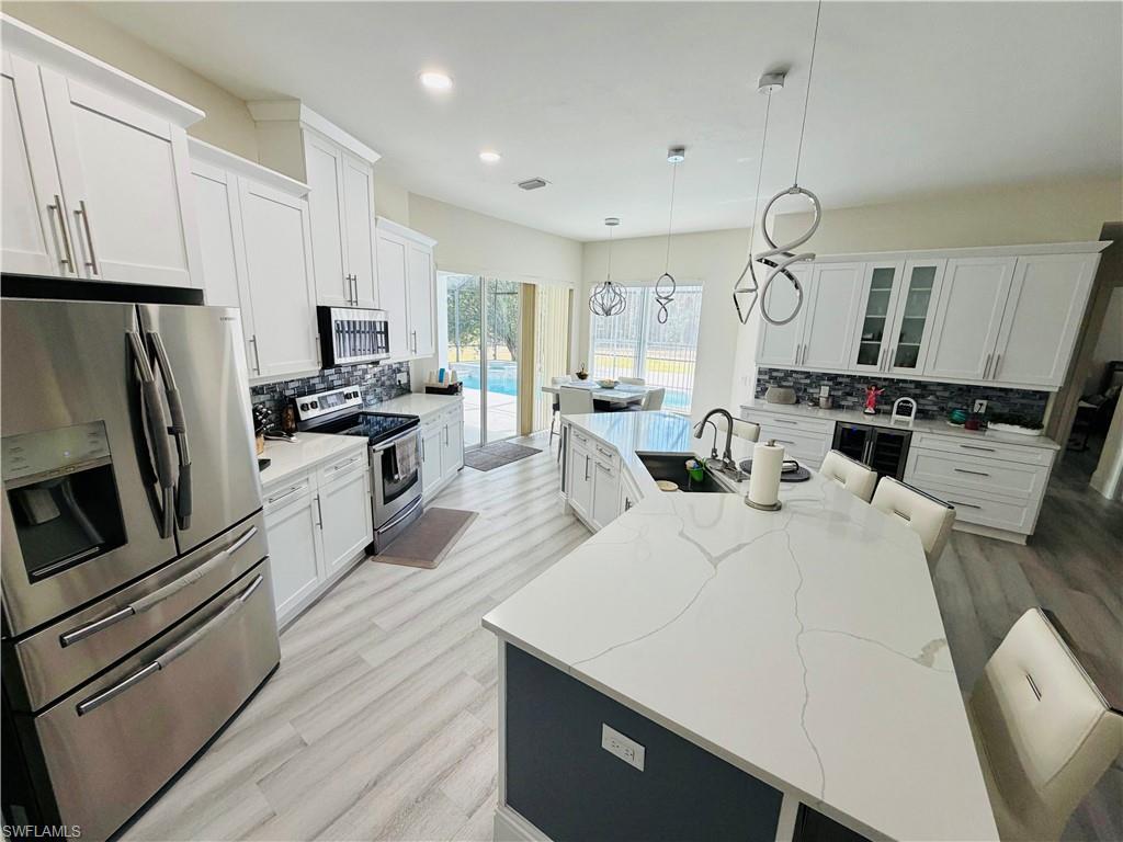 Kitchen with stainless steel appliances, white cabinets, a center island with sink, and light wood-style floors