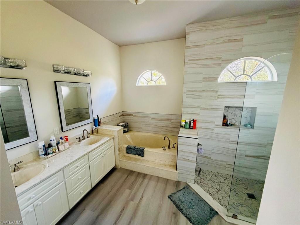 Bathroom with double vanity, a marble finish shower, light wood finished floors, and a garden tub