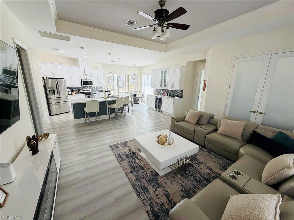 Living area featuring ceiling fan, light wood finished floors, a raised ceiling, beverage cooler, and ornamental molding