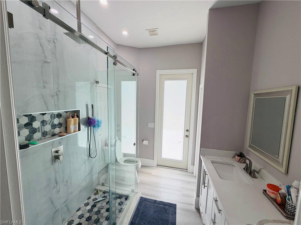 Full bath with double vanity, a marble finish shower, and light wood-style flooring