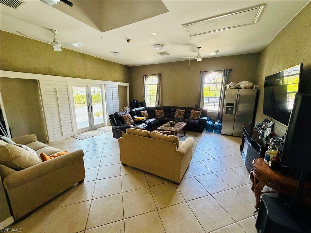 Living area with ceiling fan, french doors, plenty of natural light, light tile patterned floors, and a textured wall