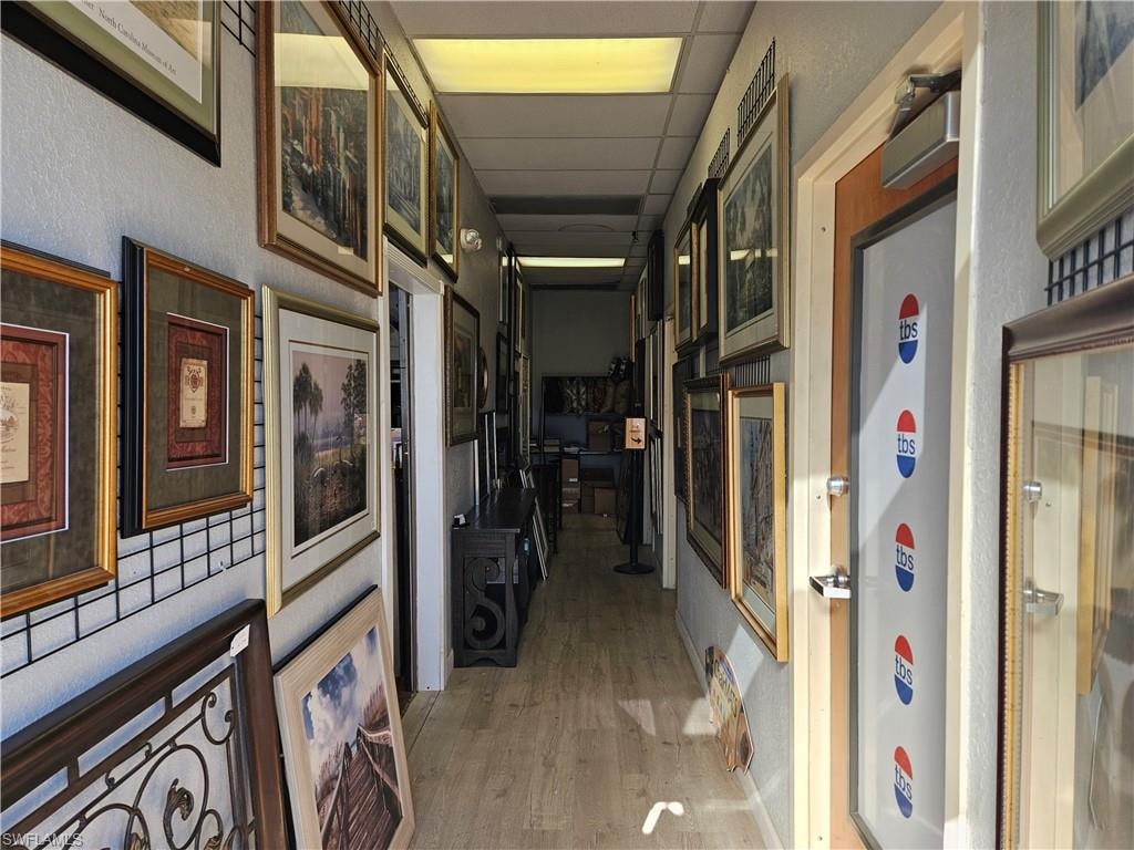 Hall featuring a paneled ceiling, light wood-style flooring, and a textured wall