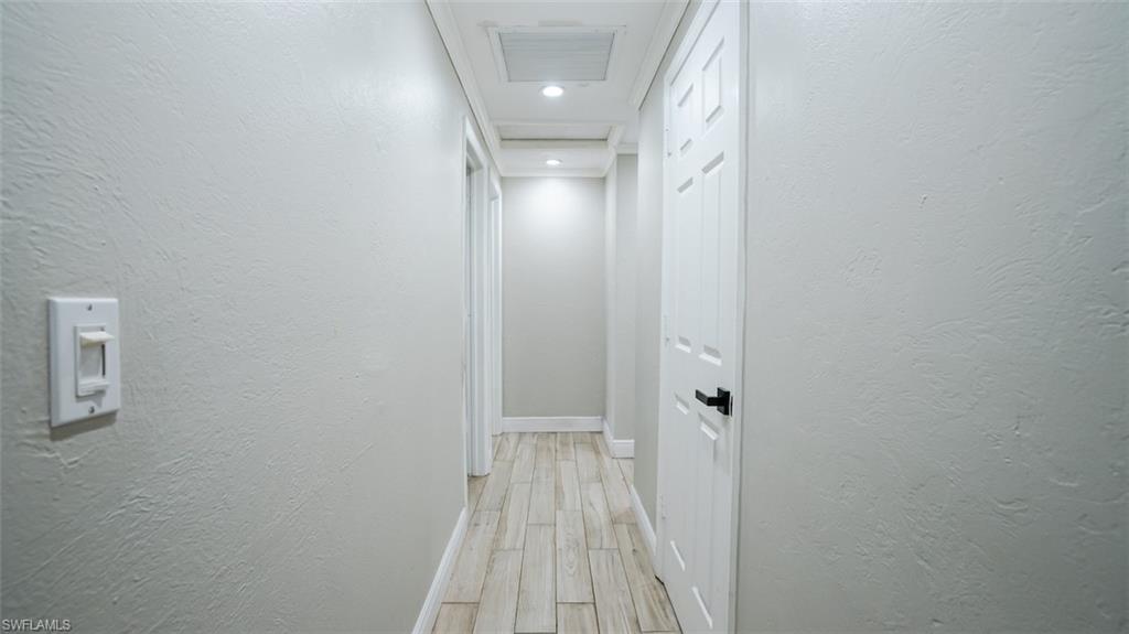 Hall featuring a textured wall, light wood finished floors, and recessed lighting