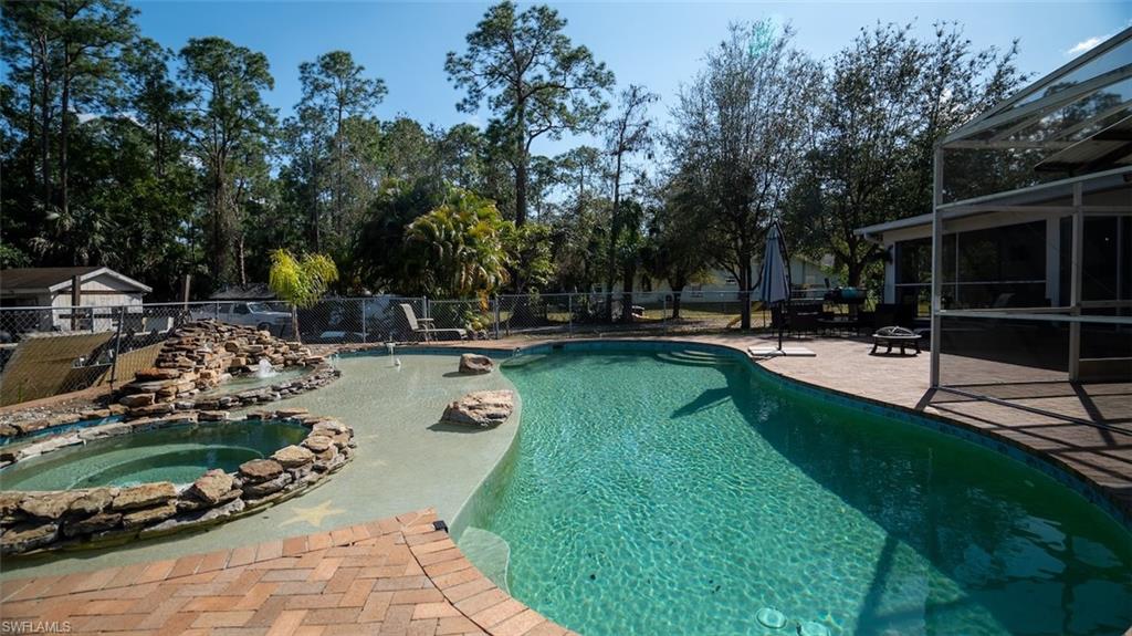 View of swimming pool with patio surround, glass enclosure, a fenced backyard, a sunroom, and an in-ground hot tub