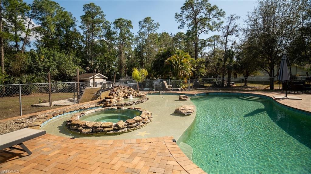 View of pool with patio surround, a fenced backyard, an in-ground hot tub, and view of wooded area