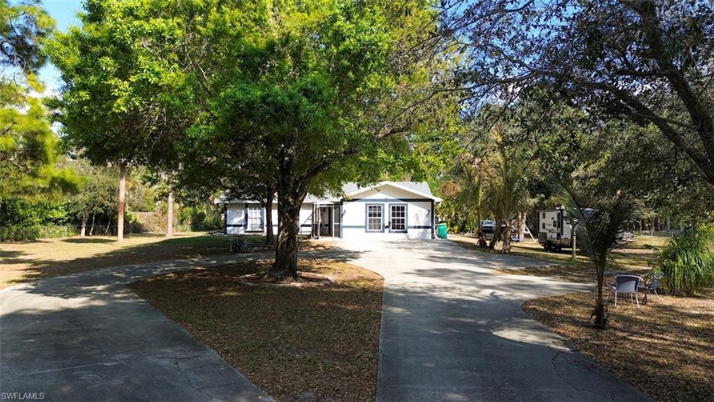 View of front of property with concrete driveway, view of wooded area, and a front yard