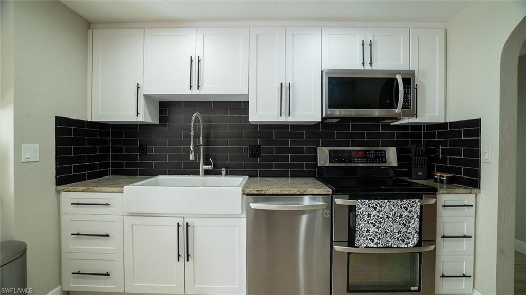 Kitchen with stainless steel appliances, white cabinets, light stone counters, arched walkways, and tasteful backsplash