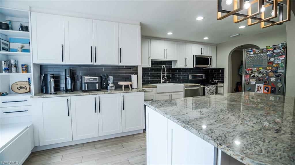 Kitchen featuring white cabinetry, open shelves, arched walkways, stainless steel appliances, and light stone counters
