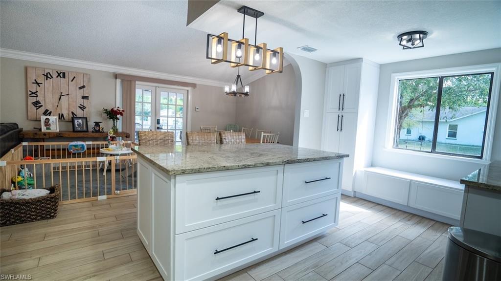 Kitchen with white cabinets, light stone counters, wood finish floors, decorative light fixtures, and a center island