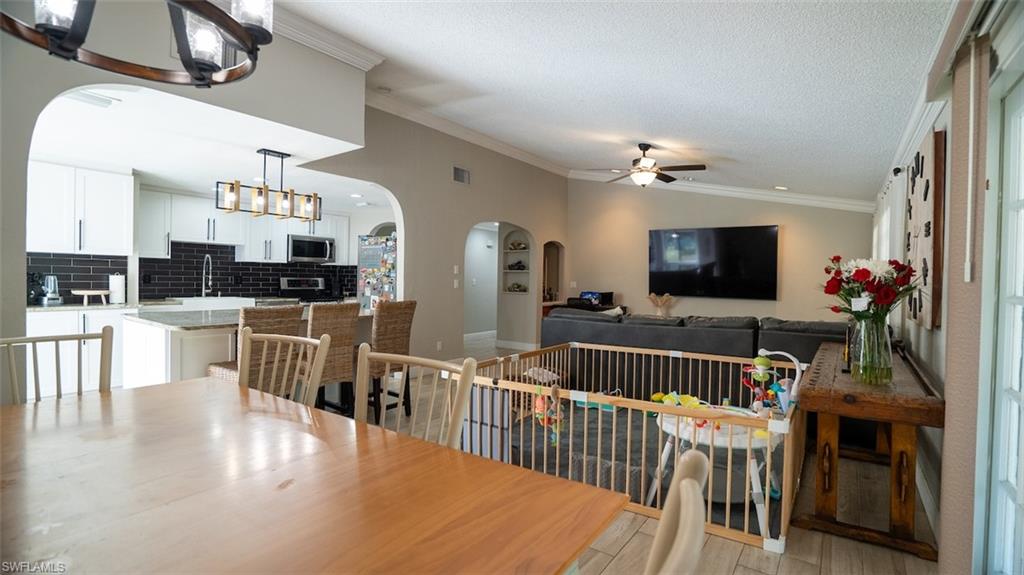 Dining area with arched walkways, hanging lights, crown molding, wood tiled floors, and a ceiling fan