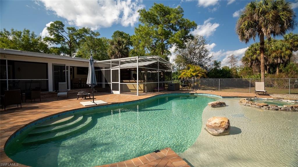 View of pool featuring patio surround, an in-ground hot tub, a lanai, a sunroom, and a fenced backyard