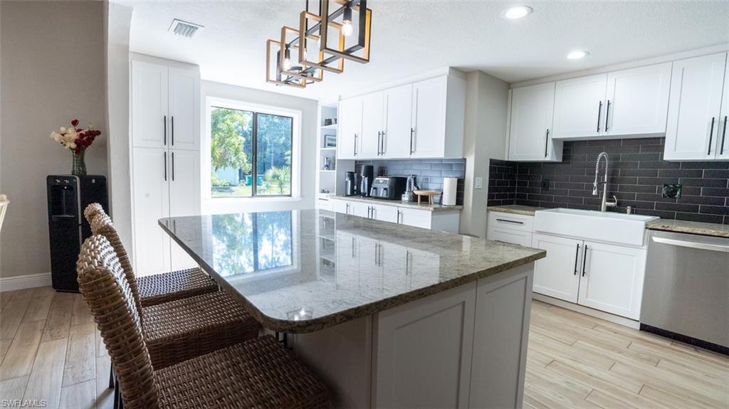 Kitchen with light stone counters, dishwasher, light wood-style flooring, tasteful backsplash, and two tone cabinets