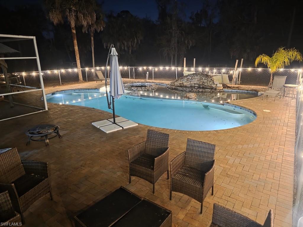 Pool at night featuring a patio and a fenced backyard