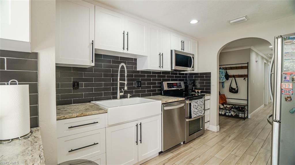 Kitchen with stainless steel appliances, white cabinets, arched walkways, recessed lighting, and crown molding