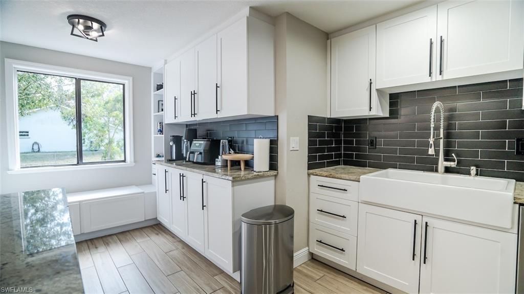Kitchen featuring white cabinets, wood tiled floors, open shelves, light stone countertops, and backsplash