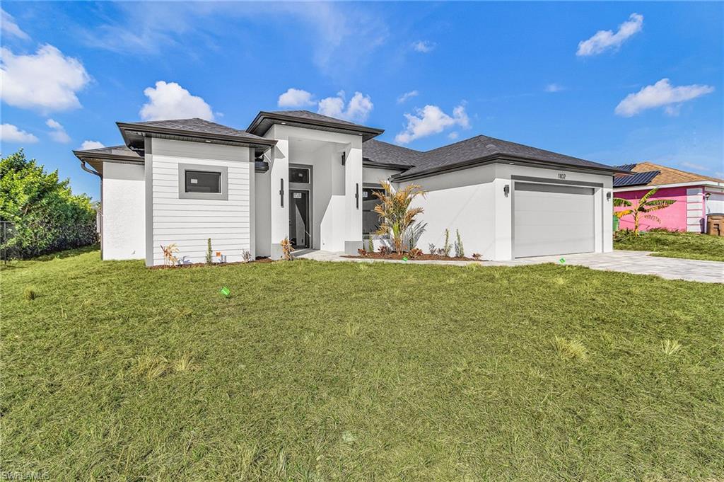Prairie-style home featuring a front yard, an attached garage, driveway, and stucco siding