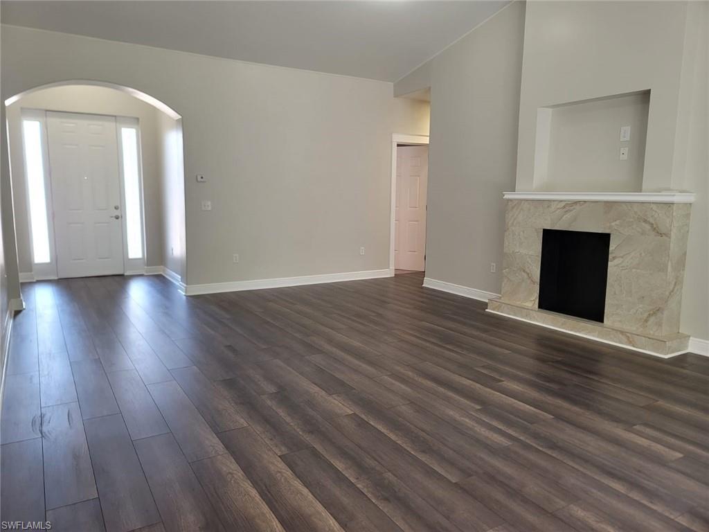 Unfurnished living room featuring arched walkways, dark wood-style floors, vaulted ceiling, and a premium fireplace