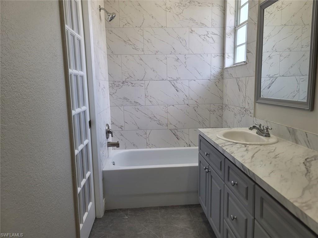 Bathroom with shower / bathtub combination, vanity, and a textured wall
