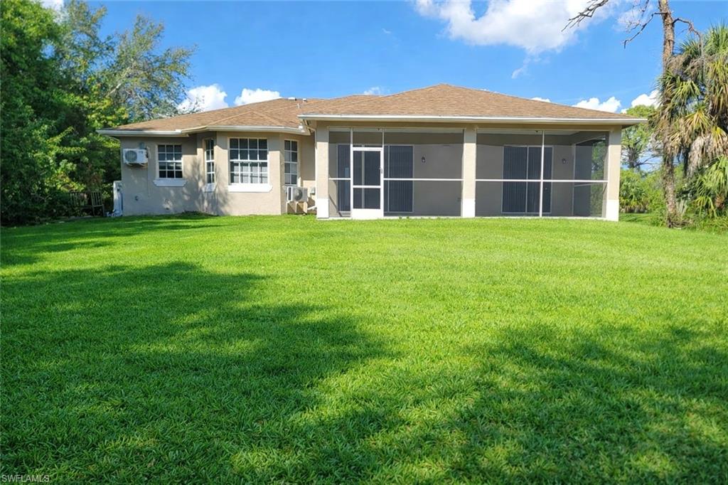 Rear view of property with a lawn, stucco siding, and a sunroom