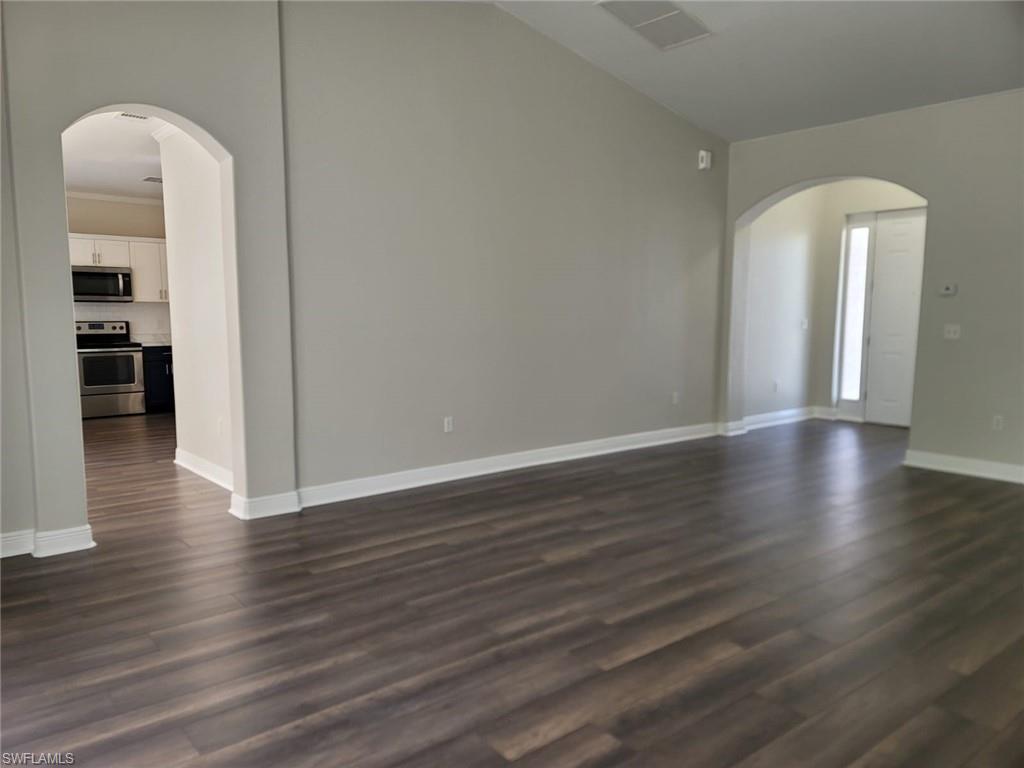 Unfurnished living room featuring arched walkways, dark wood-style flooring, and vaulted ceiling