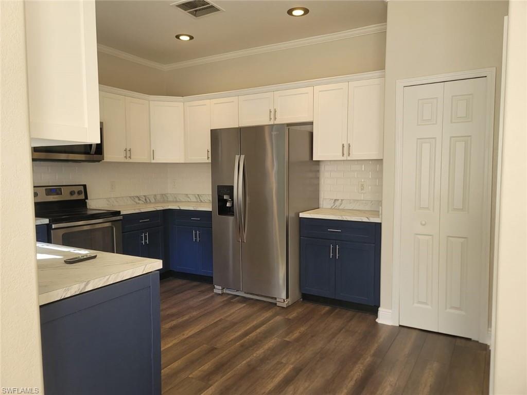 Dual tone kitchen featuring two tone cabinets, stainless steel appliances, light countertops, dark wood-style flooring, and tasteful backsplash