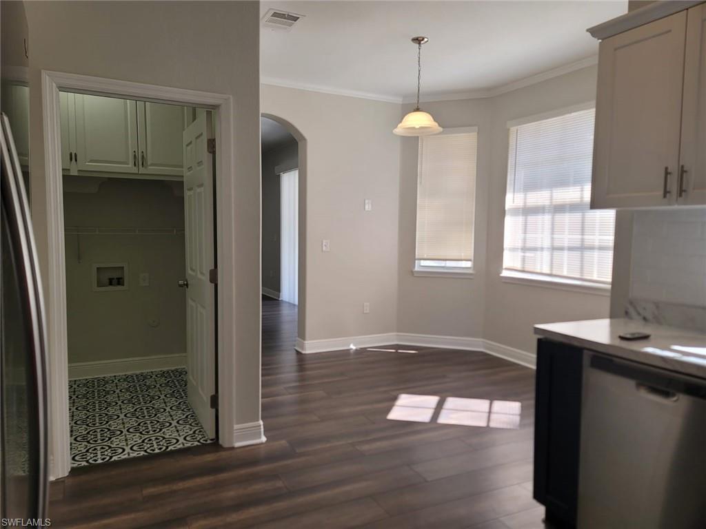 Kitchen with arched walkways, stainless steel dishwasher, ornamental molding, decorative light fixtures, and dark wood-type flooring