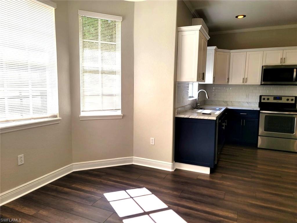Kitchen with dual tone cabinets, stainless steel appliances, light countertops, dark wood-type flooring, and backsplash