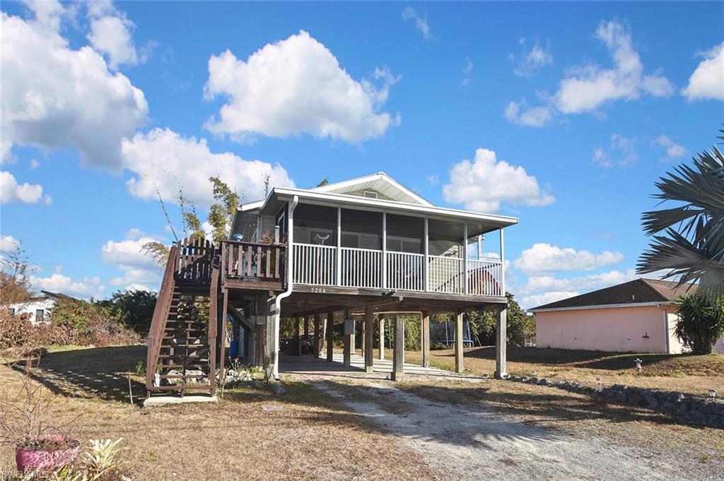 Rear view of property featuring a wooden deck, a carport, driveway, a sunroom, and a patio